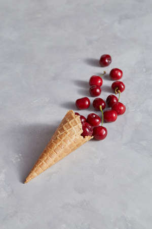 Sweet wafer cone with freshly picked red cherries on a gray background.の写真素材