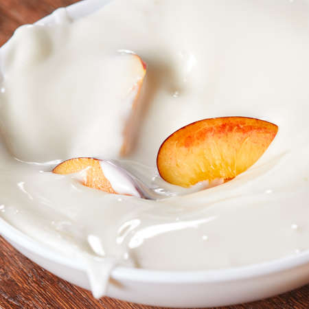 Pieces of ripe fresh peach in a ceramic bowl with fresh yoghurt on a wooden table.の写真素材