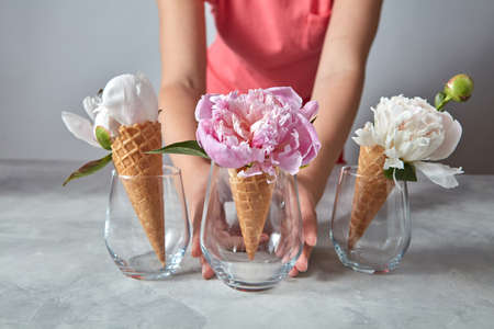 Woman hold a glass cup with beautiful pink flower pion in her hand above gray stone table.