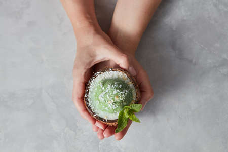 Womans hands take a halh of coconur with tasty homemade green ice cream with mint leaf on a gray concrete.の写真素材