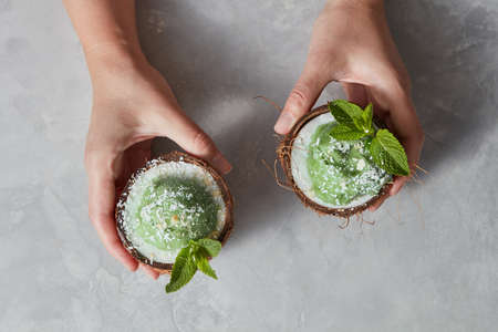 Top view of womans hands with coconut with green mint ice cream on a gray marble background.の写真素材