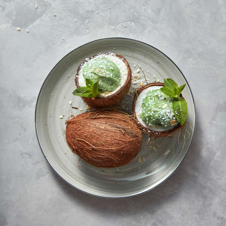 Freshly sweet green dessert in a coconut with green mint leaf and coconut chips on a plate on a concrete background.の写真素材