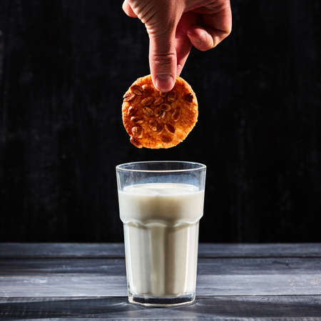 A hand dunking a cookie in a glass of milk over a black backgroundの写真素材