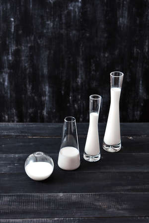 Diagonal composition of glass of different shapes and sizes filled with milk or yogurt on a black background. Natural organic dairy product.の写真素材