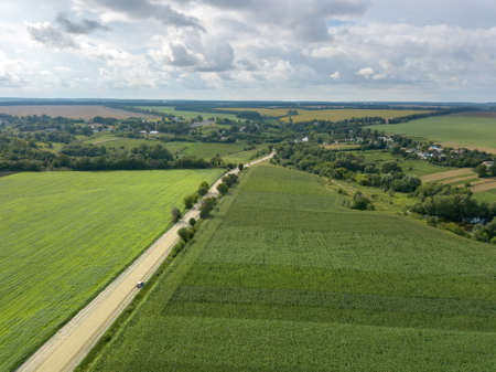 Birds eye view from drone to a rural landscape with a village, dirt road and agricultural fields of planted crops at cloude background.の写真素材