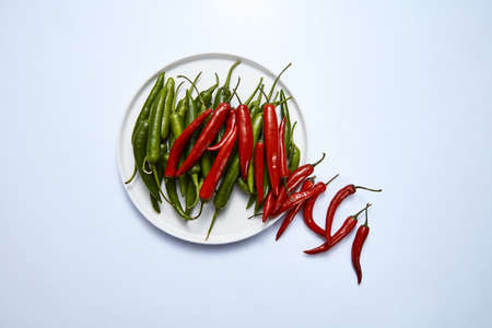 Flat lay of hot chili pepper green and red in a white plate on a white background.