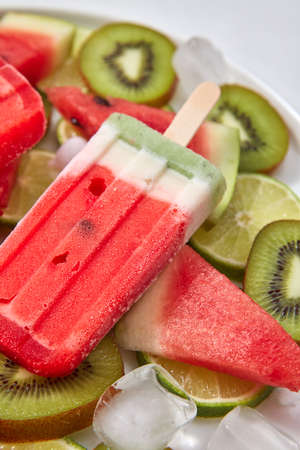 Close-up fruit frozen smoothies on a stick in the form of a piece of watermelon in a plate with ice...
