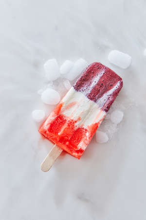 Vanilla berry sorbet on a stick with ice slices on a gray marble background with copy space. Top...