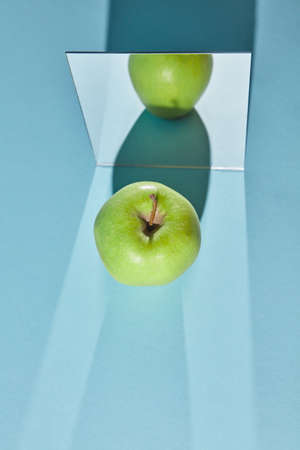 Reflection of a piece of a green apple and shadow from apple in a mirror. Long vertical shadows from...