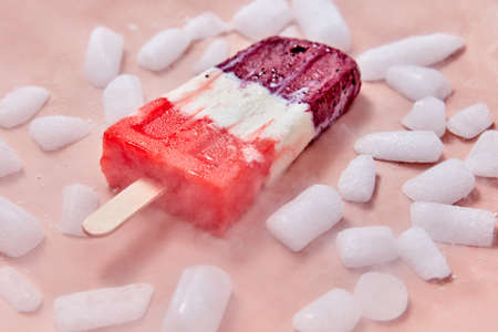 Fruit popsicle. Sweet, berry homemade ice cream on a stick with slices of ice on a pink background. Summer dessertの写真素材