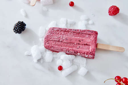 Berry apetitic organic ice cream lolly is represented on a gray marble table with different berries and ice cubes with a copy of the spaceの写真素材