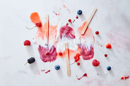 Multicolored splashes of melted ice cream sticks and juicy berries of raspberries, blueberries,...