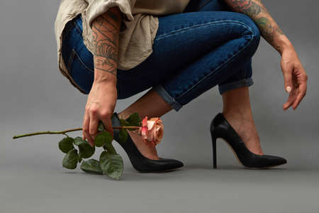 Pink flower in a girl's hand with a tattoo squatting. Young stylish girl in high-heeled shoes, and...
