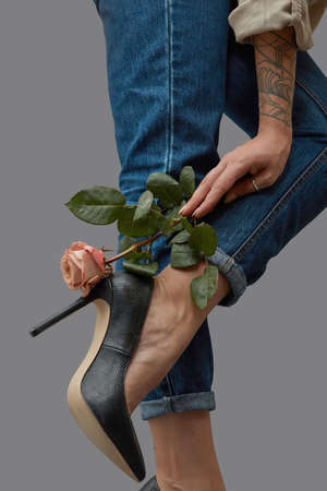 Hand of a girl with a pink flower beautifies a leg in jeans and stylish black high-heeled shoes...