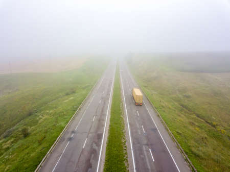 Aerial view of the road with a passing truck and a field in the autumn, foggy morning. Photo from the droneの写真素材