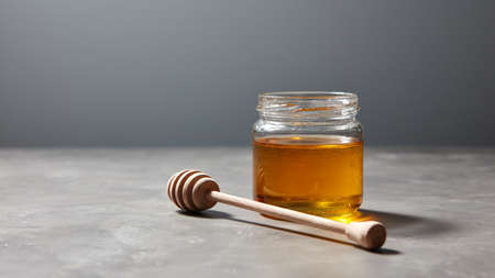 Sweet dessert - organic natural honey in a glass jar with wooden stick on a gray stone table.の写真素材