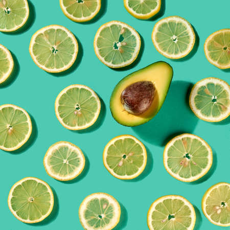 Fresh natural organic pattern with lemon fruit and single half of avocado on a pastel green...
