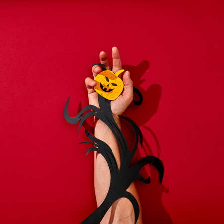A paper branch and a scary smiling pumpkin decorate a mans hand on a beautiful background with...