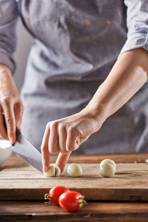 A woman in an apron slices quail eggs on a wooden board on an old wooden table. Step by Step diet saladの写真素材