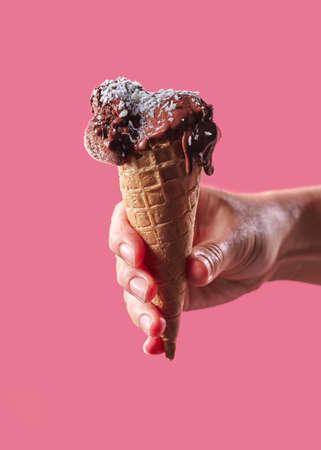 The hand of a man holds a waffle cone with fruit, ice cream decorated with coconut chips on a pink background with copy space.の写真素材