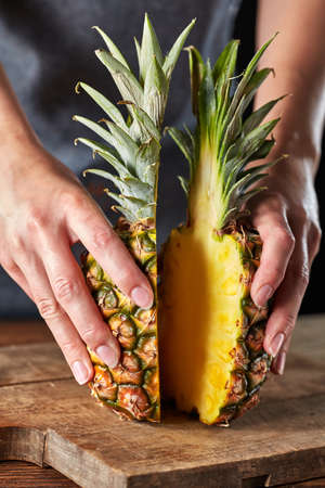 Two halves of ripe organic pineapple hold the girls hands on an old wooden board. Exotic fruitの写真素材