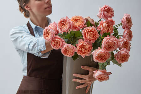 Girl florist with a big bouquet of pink roses around a gray background. The concept of a flower shopの写真素材