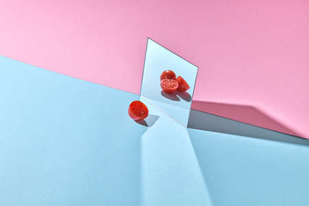 Creative composition of tomato halves and a mirror with tomatoes on a double blue-pink background with copy space.の写真素材