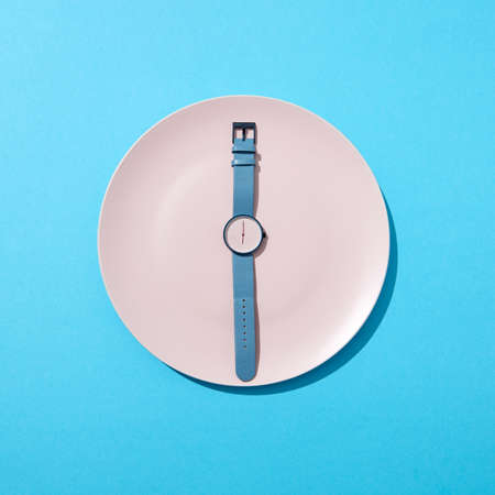 Watch with time six oclock on a white plate on a blue background. Concept of limiting the intake of food diet and weight loss. Flat lay.の写真素材