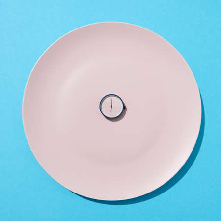 Round watch six oclock on white plate on a blue background. Time to eat and diet concept. Place for...