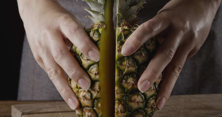 Close up view. Womans hands hold two pieces of juicy fresh natural organic pineapple on a wooden background.の写真素材