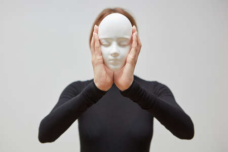 Attractive girl in a black jumper holds gypsum mask sculpture instead of face on a white background....