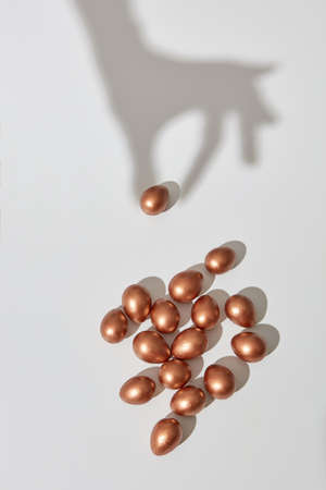 The shadow of the hand takes a golden painted egg on a gray background with copy space for text. Profit concept. Flat layの写真素材