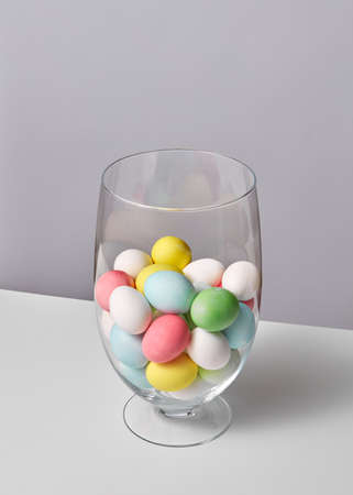Multi-colored painted eggs in a glass vase on a gray background with space for text. Easter conceptの写真素材