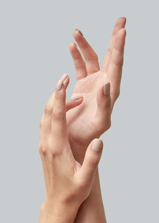 Closeup of beautiful woman hands with light manicure on nails on a gray background. Massage of hands using cream.の写真素材
