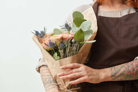 Fresh flowers living coral roses and eryngium as a congratulate bouquet in girls hand with tattoo, copy space. Post card for Mothers Day.の写真素材