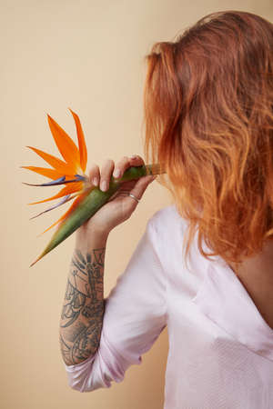 Strelitzia flower decorating the shoulder of a red-haired girl with a tattoo on a beige background with space for text. Creative layoutの写真素材