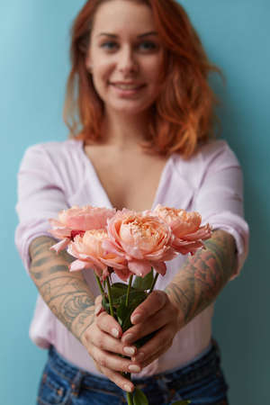 A smiling girl with a tattoo gives a bouquet of pink roses around a blue background with copy space. Mothers Day Giftの写真素材