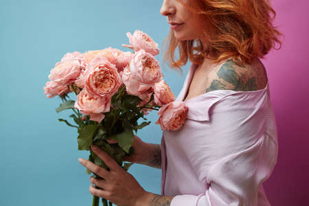Gentle pink roses in the hands of a girl with a tattoo on a double pink blue background with copy...