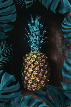 Fresh pineapple on an old wooden background decorated with a frame of palm leaves. Tropical fruitの写真素材