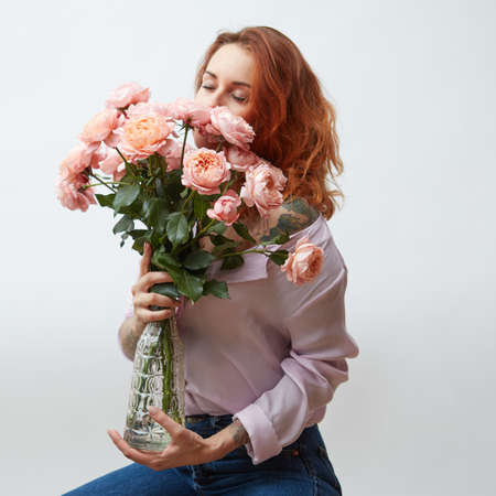 Sexy girl with a bouquet of delicate pink roses in a transparent vase on a gray background with copy space. St. Valentines Dayの写真素材