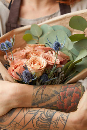 Close up of fresh tender roses and eryngium in a womans hands with tattoo. Congratulation concept of Mothers Day.の写真素材