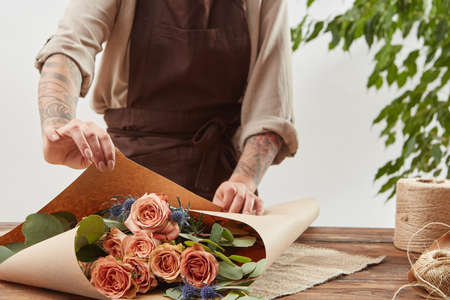 Gardener girl make bouquet for a holiday from living coral roses and branches of green leaf on a wooden table on a light background. Mothers Day.の写真素材
