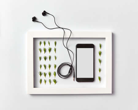 Frame with organic pine needles pattern, smartphone mock-up and headphones on a light background.