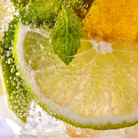 Green leaf of mint, pieces of lemon and lime with bubbles in a transparent glass. Macro photo of summer cold mojitoの写真素材