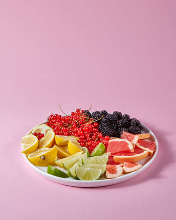 Red currants, mulberries and pieces of lemon, lime, grapefruit in a plate on a pink background with copy space. Set for the preparation of summer vitamin drinkの写真素材