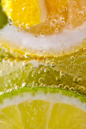 Pieces of citrus fruits of lemon and lime with bubbles in a glass of water. Macro photo of summer drinkの写真素材