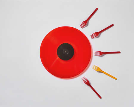 Creative composition with red vinyl record and plastic colored forks on a gray background. Concept...