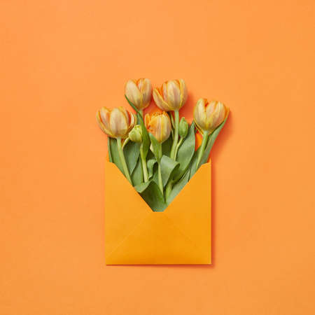 Post card with bouquet of tulips in craft envelope on an orange background.の写真素材