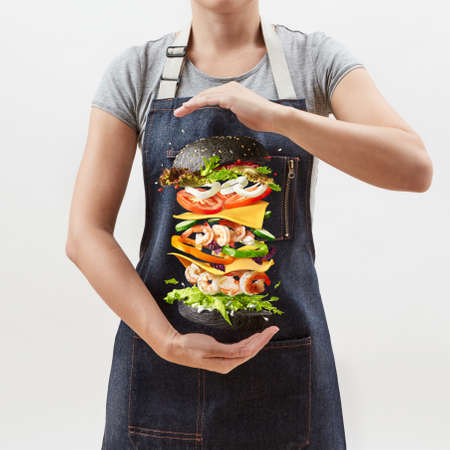 Woman holds a flying homemade burger from fresh organic ingredients on a light background.の写真素材