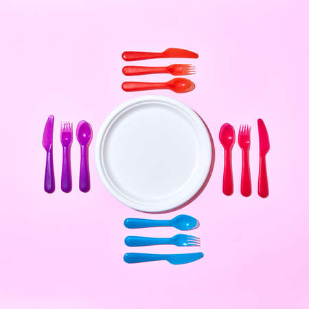 Multicolored plastic utensil around white plate on a light pink.の写真素材
